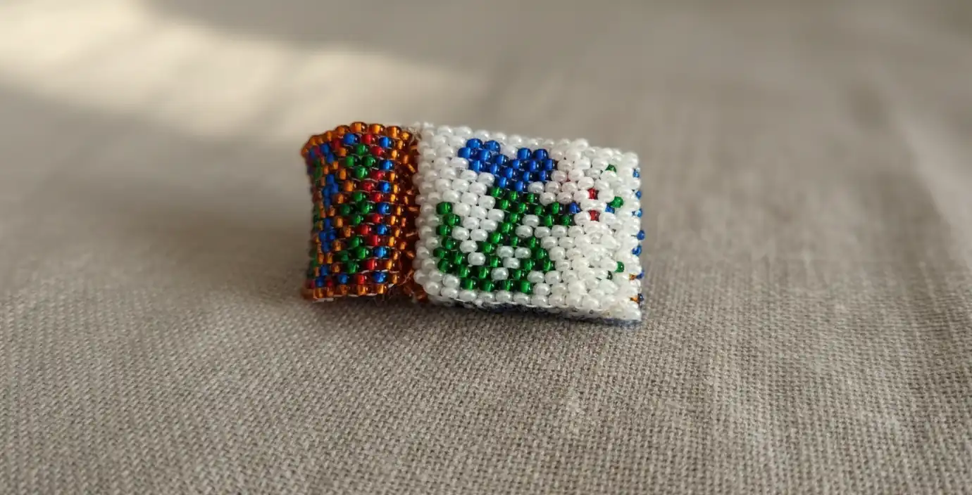 Mini-livre décoratif tissé en perles de rocaille, symbolisant l'histoire et les secrets de cet artisanat ancestral.