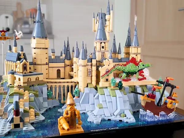 Détail de la maquette LEGO de Poudlard avec un petit dragon artisanal en perles de rocaille vert brillant et des figurines fantastiques au premier plan.