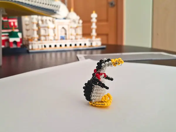 Vue de profil d'une figurine de pingouin en perles de rocaille, montrant son écharpe rouge en relief et son corps bombé. Une création artisanale minutieuse posée sur un support neutre.